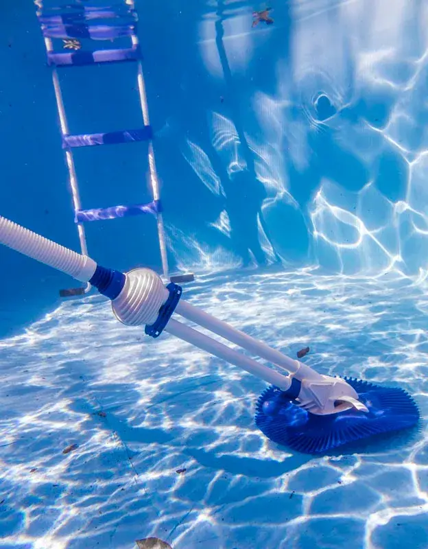 19001-2 | PisciManía Underwater pool cleaner with a hose and blue wheel-like base resting on the pool floor beside a metal ladder.