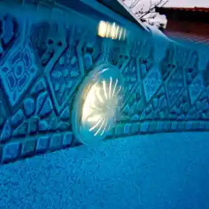 pled2-3 | PisciManía Close-up of a blue tiled pool wall with a round underwater light emitting a soft glow.