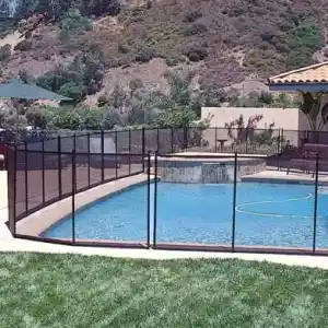 sf133-1 | PisciManía Outdoor pool area with a black metal safety fence, a spa at one end, patio seating, and a grassy lawn with hills in the background under a blue sky.