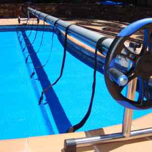 Manual pool-cleaning reel with hose laid along the edge of a blue swimming pool.